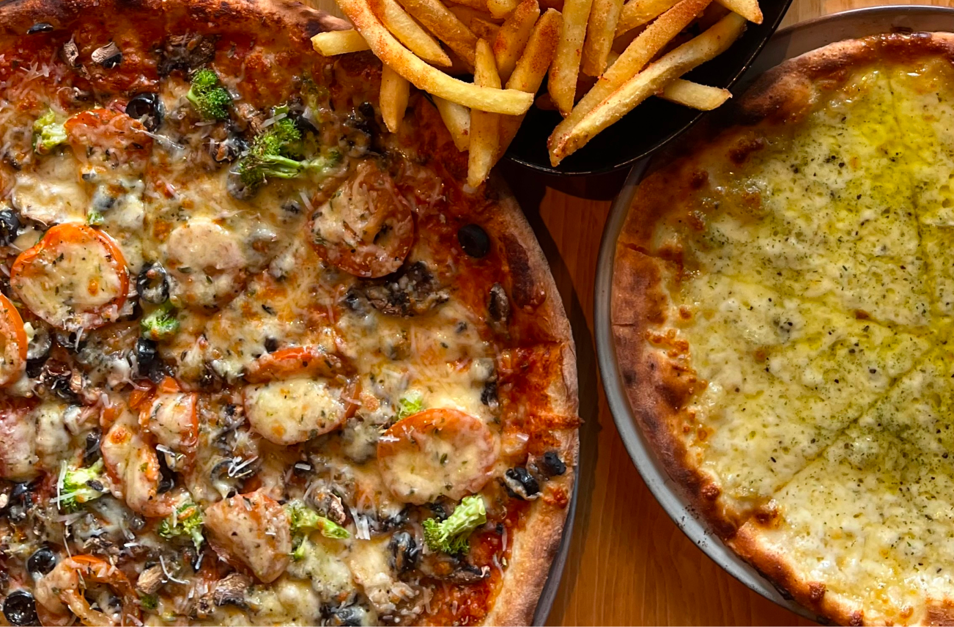 A close up of two pizzas and french fries
